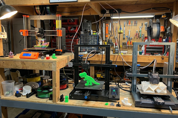Three budget 3D printers under 500 dollars arranged on workshop shelving